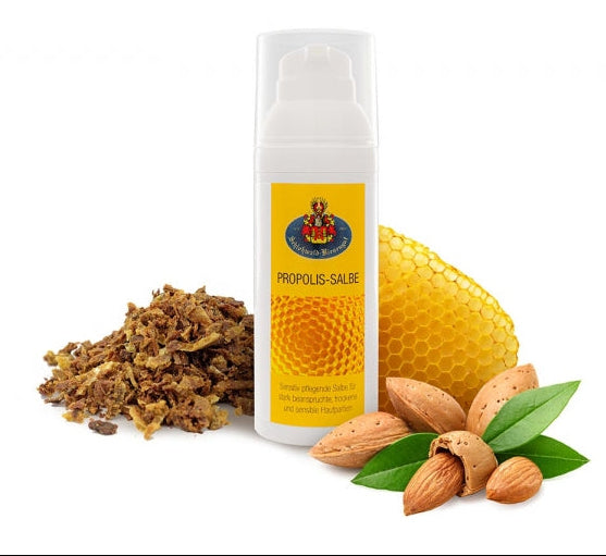 Propolissalbe in einem weißen Airlessspender mit gelbgoldenem Etikett. Rechts daneben eine Bienenwabe und links Propolis.