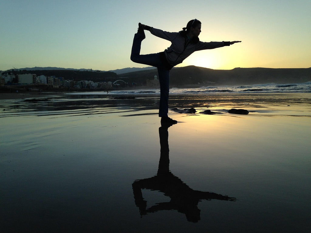 Frau macht Yoga am Strand bei Sonnenuntergang