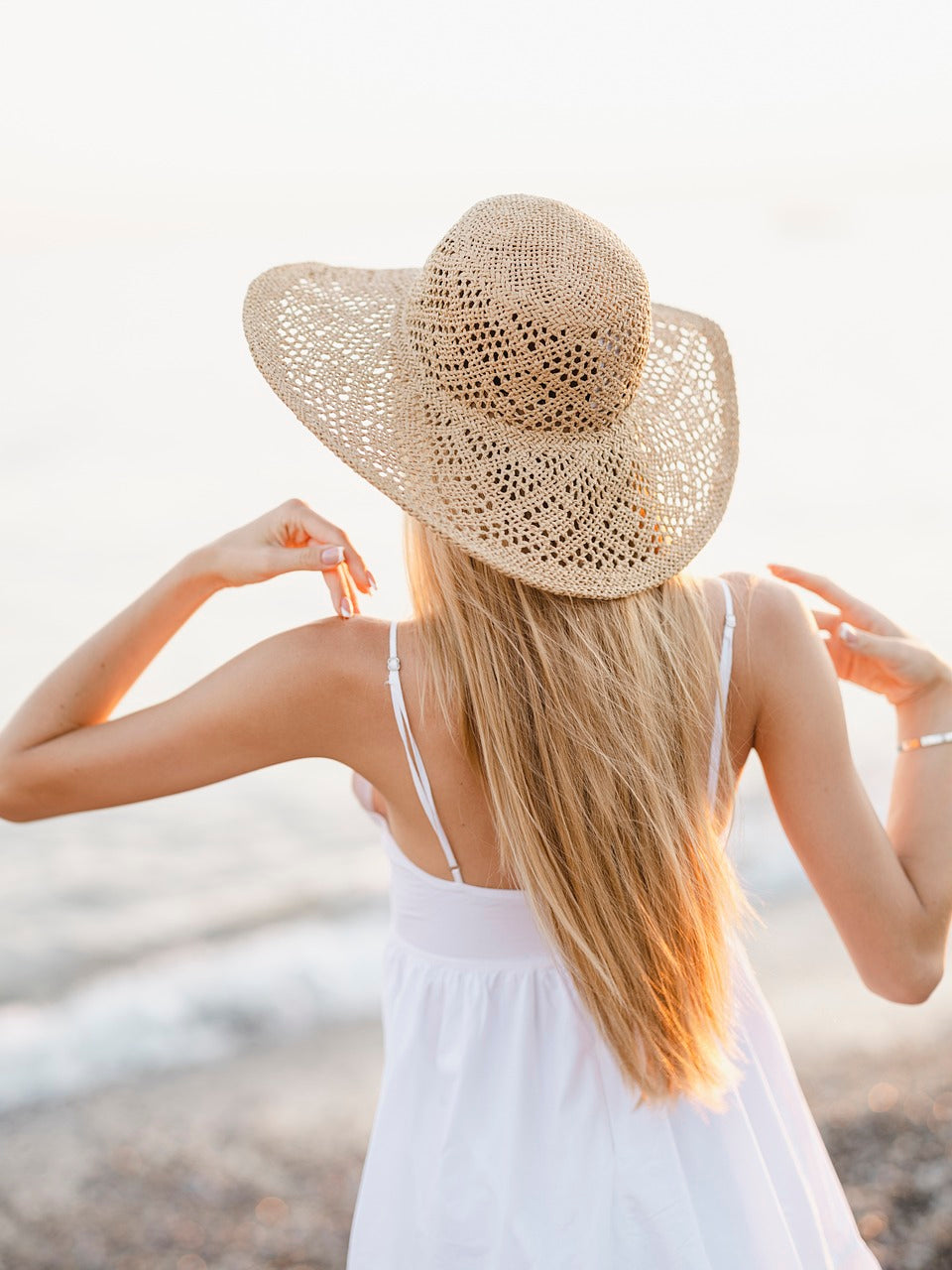 Blonde Frau mit langen Haaren und Strohhut am Strand