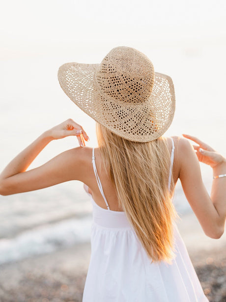 Blonde Frau mit langen Haaren und Strohhut am Strand