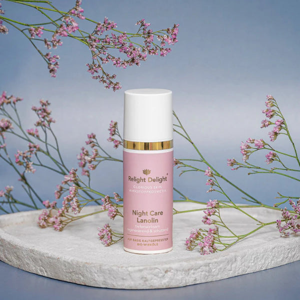 Roséfarbene Tube,sehr edel mit gold und weißer Aufschrift: Glorious Skin - Night Care Lanolin, tiefenwirksam regenerierend und schützend,  50ml von Relight Delight auf hellem Stein stehend mit rosa Blüten im Hintergrund