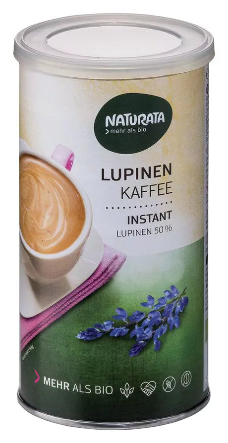 Eine zylindrische Dose Naturata Lupinen Kaffee Instant ist vor einem neutralen, hellen Hintergrund abgebildet. Die Dose hat ein Etikett, das oben das grüne Naturata-Logo zeigt und den Text 'LUPINEN KAFFEE INSTANT LUPINEN 50%'. Ein Teil einer Kaffeetasse mit cremigem Kaffee Latte und ein pinkes Tuch sind auf dem Etikett zu sehen, zusammen mit blauen Lupinenblüten auf einem grünen Feld im unteren Bereich. Unten auf der Dose steht 'MEHR ALS BIO' und verschiedene Symbole.