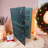 Adventskalender mit 24 Seifenträume Petrolfarben mit Aufschrift : Frohe Weihnachten und eine kleine Auszeit für dich. Rechts sieht man einen Kranz mit roten Weihnachtskugeln und links im Bild  hübsch dekoriert mit goldener Geschenkverpackung