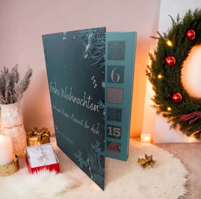 Adventskalender mit 24 Seifenträume Petrolfarben mit Aufschrift : Frohe Weihnachten und eine kleine Auszeit für dich. Rechts sieht man einen Kranz mit roten Weihnachtskugeln und links im Bild  hübsch dekoriert mit goldener Geschenkverpackung