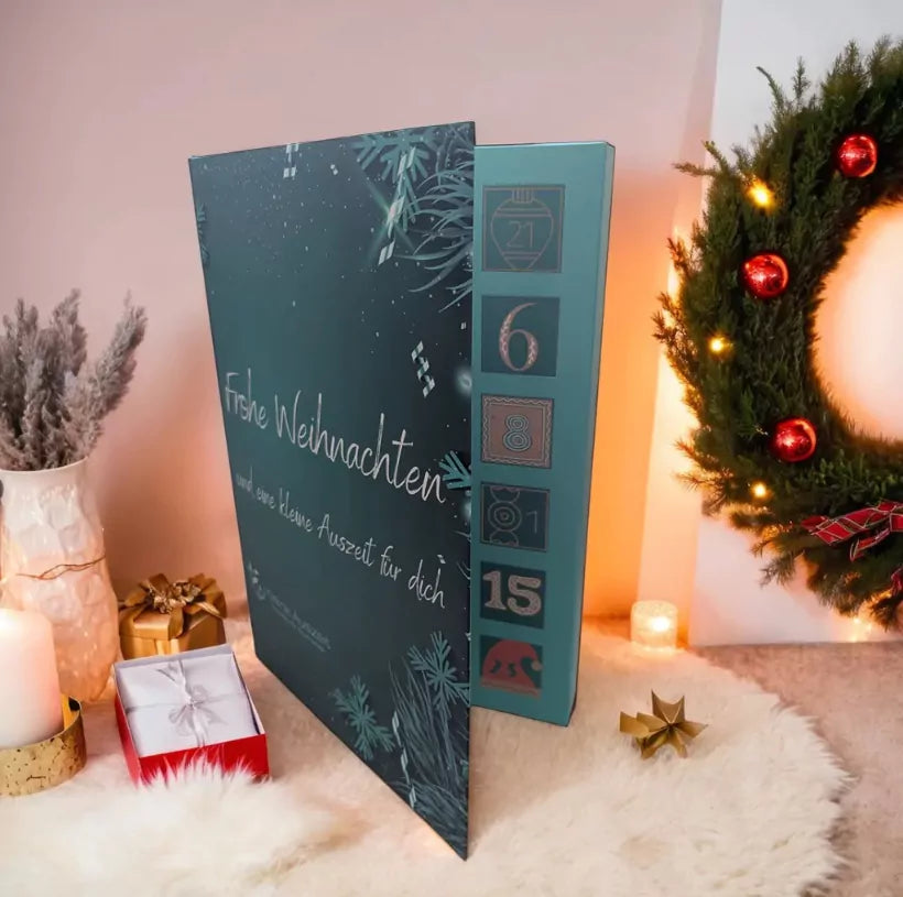 Adventskalender mit 24 Seifenträume Petrolfarben mit Aufschrift : Frohe Weihnachten und eine kleine Auszeit für dich. Rechts sieht man einen Kranz mit roten Weihnachtskugeln und links im Bild  hübsch dekoriert mit goldener Geschenkverpackung