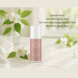 Im Zentrum steht eine roséfarbene Tube mit dem Produkt Beauty Basics - Cream light. Die Flasche befindet sich auf einer weißen Holzoberfläche. Um die Flasche herum sind weiße Blüten und grüne Blätter arrangiert, die eine sanfte und natürliche Atmosphäre schaffen. Im Hintergrund ist eine unscharfe Darstellung einer Pflanze in einer Vase zu sehen. Rechts neben der Flasche steht der Text "Leichte Textur, Für einen klaren Teint, Mit wertvollen, kaltgepressten Ölen, Perfekt für junge Haut".