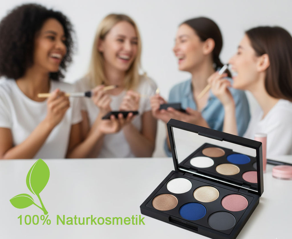 Eine offene Lidschattenpalette steht dezent auf einem weißen Tisch. Im unscharfen Hintergrund lacht eine Gruppe von vier Frauen, die sich gemeinsam schminken und dabei Spaß haben.