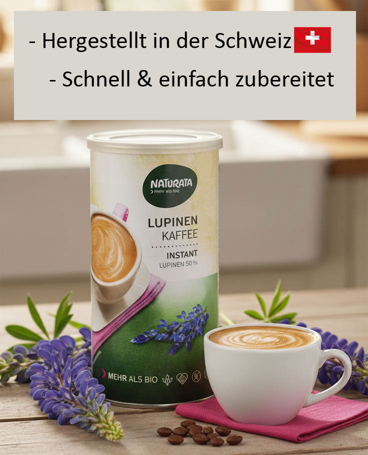 Eine Dose Naturata Lupinen Kaffee Instant steht auf einem rustikalen Holztisch. Links und rechts von der Dose sind frische, lilafarbene Lupinenblüten arrangiert. Vor der Dose steht eine weiße Tasse mit einem liebevoll zubereiteten Kaffee Latte, der auf einem pinken Tuch platziert ist. Vereinzelt liegen Kaffeebohnen auf dem Tisch. Im unscharfen Hintergrund ist eine helle Küchenumgebung mit einem Fenster und einer Spüle zu erkennen.