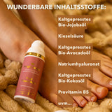 Auf dem Bild sieht man ein Paar entspannte, gepflegte Füße, die auf einer weichen, beigefarbenen Unterlage ruhen. Daneben steht der Relight Delight – Glorious Skin Foot Repair Balm, ein hochwertig wirkender Tiegel in warmen Naturtönen.
Im Hintergrund sind die natürlichen Inhaltsstoffe des Produkts in deutscher Sprache aufgeführt, darunter kaltgepresstes Bio‑Jojobaöl, Bio‑Avocadoöl, Bio‑Kokosöl, Kieselsäure, Natriumhyaluronat und Provitamin B5.
