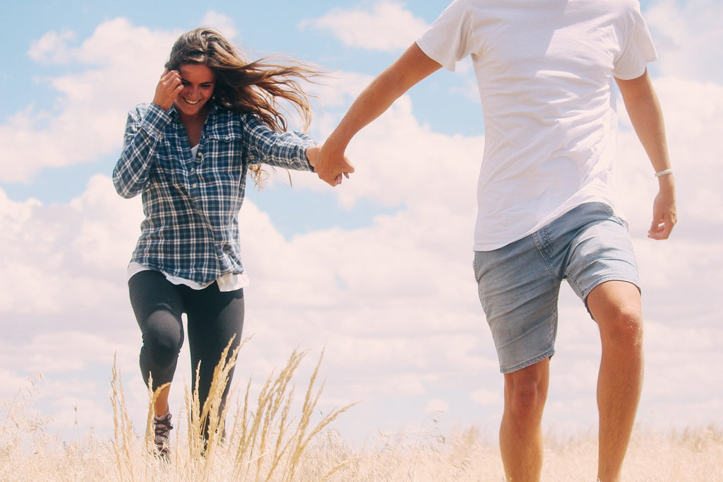 Mann und Frau laufen hand in hand glücklich über eine Wiese
