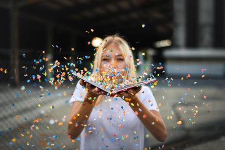 Blonde Frau pustet Konfetti aus einem Buch