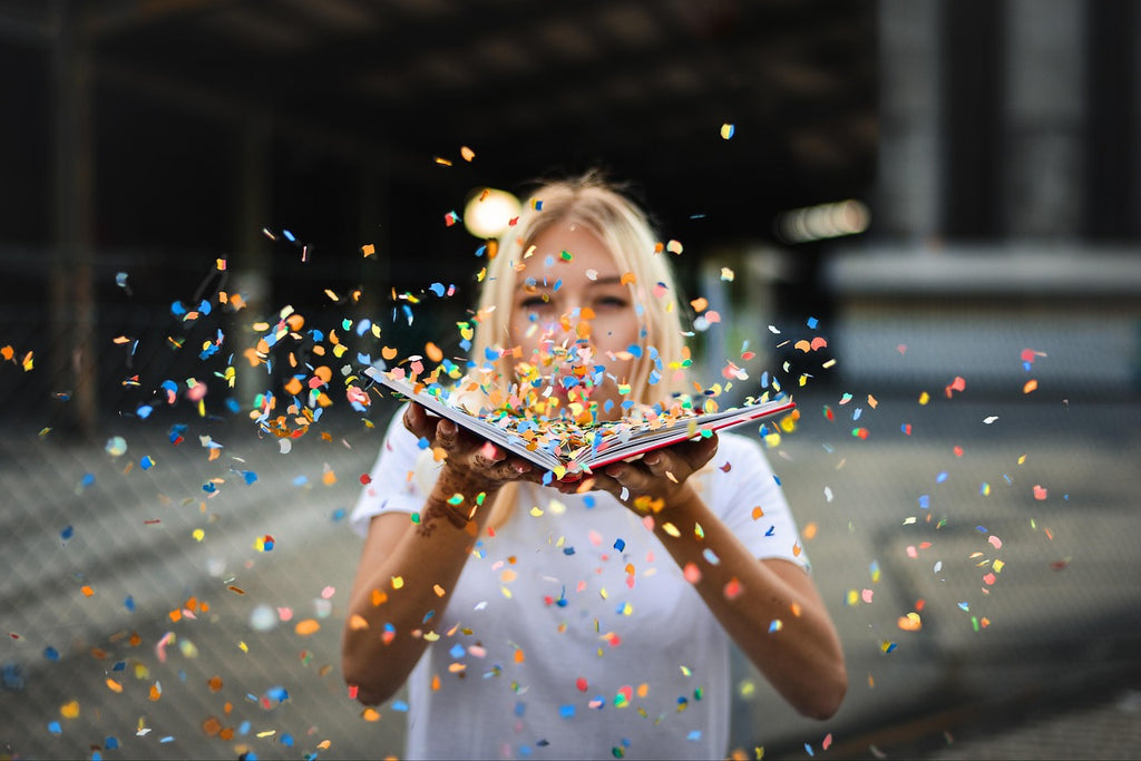 Blonde Frau pustet Konfetti aus einem Buch
