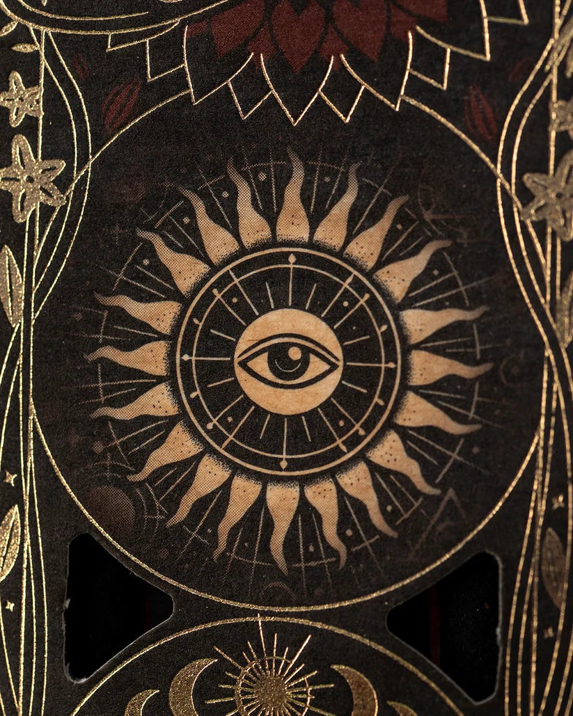 Nahaufnahme des Verpackungsmotivs mit einem zentrierten Auge in einem flammenden Sonnenrad mit goldenen Strahlen und Ornamenten.