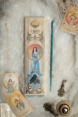 Flachliegendes Arrangement des Sagrada Madre Tarot Angels Räucherwerks auf weißem Fell mit Verpackung, blauem Stäbchen, zwei Engelkarten und antik aussehenden Schlüssel-Dekorationen.