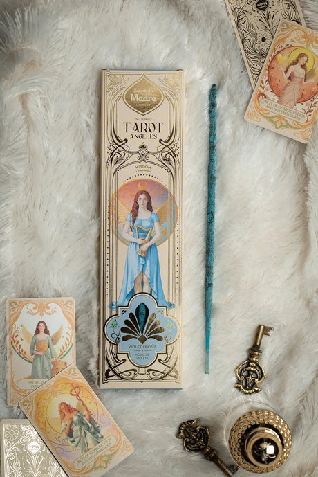 Flachliegendes Arrangement des Sagrada Madre Tarot Angels Räucherwerks auf weißem Fell mit Verpackung, blauem Stäbchen, zwei Engelkarten und antik aussehenden Schlüssel-Dekorationen.