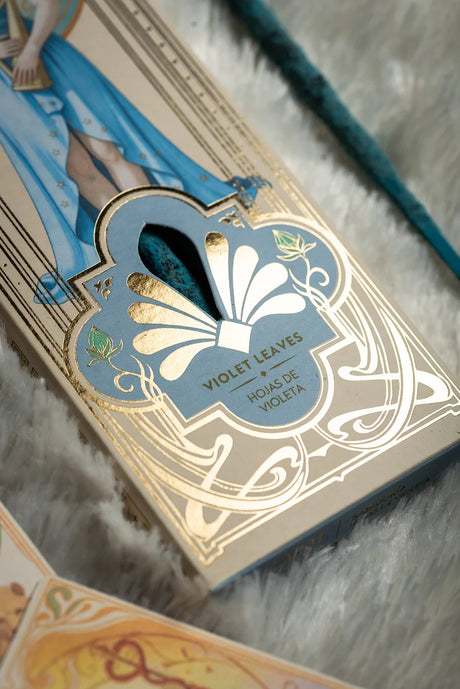 Nahaufnahme der Unterseite der Verpackung mit goldenem Ornament-Muster, Sichtfenster für die blauen Stäbchen und der Duftbezeichnung Violet Leaves / Hojas de Violeta.
