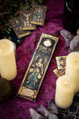 Sagrada Madre Tarot de Marsella Räucherpackung auf lila Textiluntergrund, umgeben von brennenden weißen Kerzen, Tarotkarten und Kristallen.