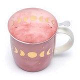 Rosa Teetasse mit Deckel und Sieb, verziert mit goldenen Mondphasen.  Ansicht von oben auf den Deckel .Die Tasse hat einen weißen Henkel und ein metallisches Teesieb.